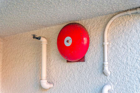 Red fire alarm bell on a painted white textured wall in San Francisco, Californiaの写真素材