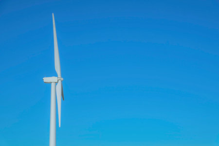 Close up side view of windmills with blue sky background on a sunny day. The towering innovative...