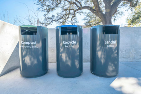 Black trash cans for segregation of wastes at Waterloo Park in Austin Texas. Garbage bins with labels for compost, recycle and landfill against concrete wall, trees and blue sky.の写真素材