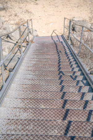 Outdoor staircase against dry sunlit ground near Lake Austin in Texas. Looking down from the top of a public stairway with dirty metal steps and rusty metal railings.の写真素材