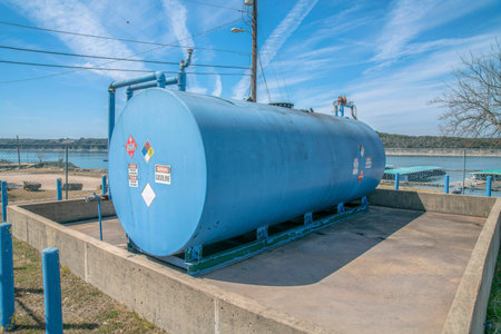 Blue cylindrical propane gas tank against Lake Austin and cloudy blue sky. A liquefied petroleum gas storage container against blue water and bright skyscape in Texas.の写真素材