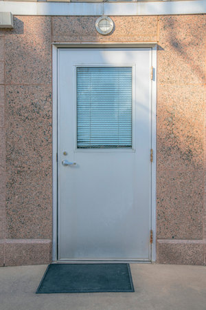 White door with glass pane against reddish concrete wall of an old building. Views in Austin Texas with close up on a closed door that has white blinds behind the glass panel.の写真素材