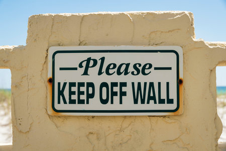 Please Keep Off Wall sign against white textured wall in Destin Florida. Close up view of a sign board informing people to avoid touching the wall.の写真素材