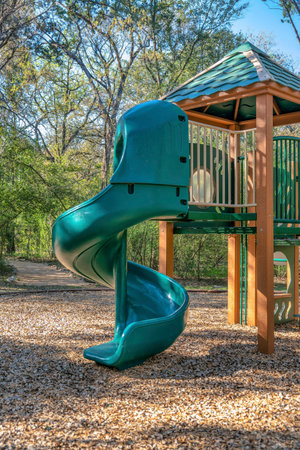 Austin, Texas- Spiral slides on a community playground. View of a slide for kids against the view of a trail in the middle of a forest at the background.の写真素材