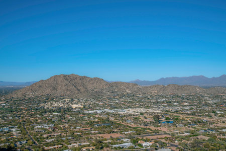 Overlooking view of a town area from the hiking trail at Camelback Mountain at Phoenix, Arizona. View of buildings and roads below near the mountains against the blue sky background.の写真素材