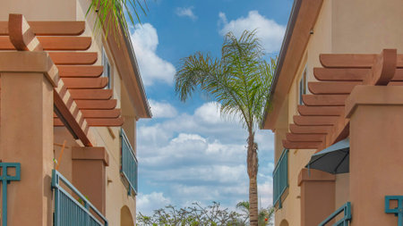 Panorama White puffy clouds Two identical mediterranean houses across each other at La Jolla, Callifornia. Houses exterior with blue metal railings and potted plants on the balconies and trees outdoor.の写真素材