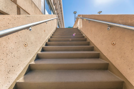 View from the bottom of staircase outside a building with blue sky and sunlight. Outdoor stairway with concrete steps and metal railings in downtown Austin Texas.の写真素材
