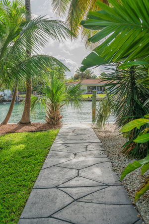 Concrete pavement at the shore of the bay near the dock in Miami, Florida. Pathway near the lawn on the left and plants on the right with a view of dock posts at the background.の写真素材