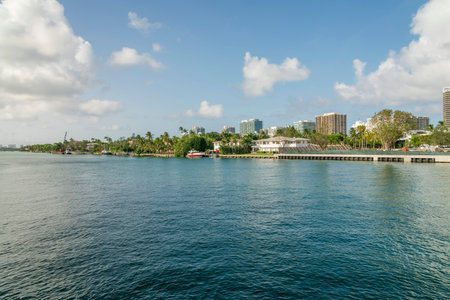 Views of buildings across the ocean under the calm sky with fluffy white clouds- Miami bay, Florida. There is a reflective ocean waters at the front and views of trees at the shore across.の写真素材