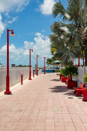 Sidewalk at the bay with contemporary red street lights, benches, and planters in Miami, FL. There is a fence near the water with boats on the docks across the benches near the trees and plants.の写真素材