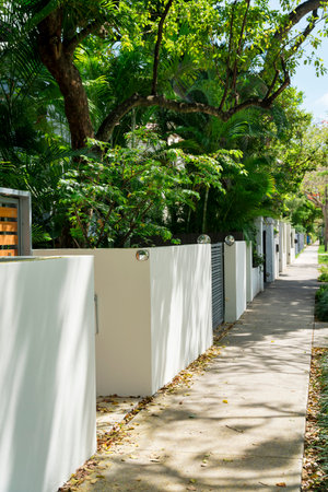 Concrete path outside the concrete walls of residences at Miami, Florida. There are painted white walls with trees behind on the left side of the walkway.の写真素材