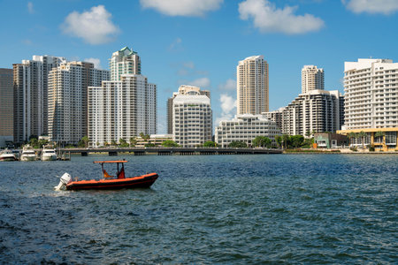Orange boat on the ocean against the cityscape view at the bay in Miami, Florida. There is water at the front with a view of a boats on the left near the bridge heading to the multi-storey buildings.の写真素材
