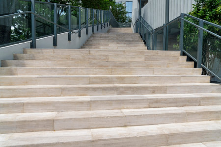 Wide outdoor stairs with glass baluster and metal bar handrails at Miami, Florida. Stairs with wood texture tiles near the plants, trees, and building on the side.の写真素材