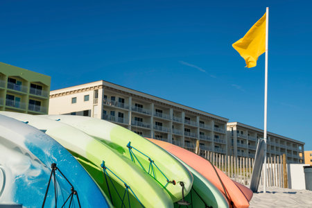Kayak rentals near the yellow flag on a pole at the front of hotel buildings in Destin, Florida. Kayaks at the front of beachfront hotels against the clear blue sky background.の写真素材