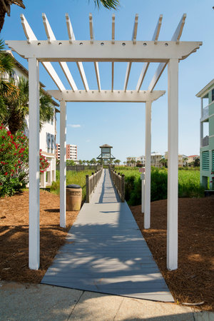 Entrance pathway with white pergola heading to a boardwalk over the grasses at Destin, Florida. Wooden pathway over the tall grasses near the residences and clear sky background.の写真素材