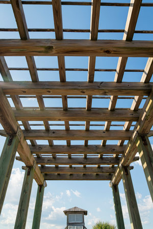 Destin, Florida- View of a wooden outdoor roof grid under the clear sky. Low angle view of a roof with wood pillars and a view of a shed at the background.の写真素材