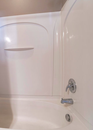 Vertical Shower tub combo kit with acrylic wall panel and white shoer curtain. Shower tub near the brown wall above the wall panel and a wall mounted faucet and shower head.の写真素材