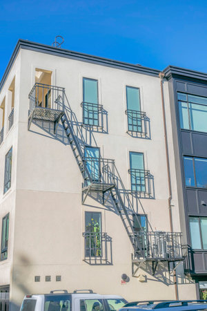 Residential building with fire exit stairway against blue sky on a sunny day. This aparment complex in San Francisco California also has white concrete wall and tall narrow windows.の写真素材