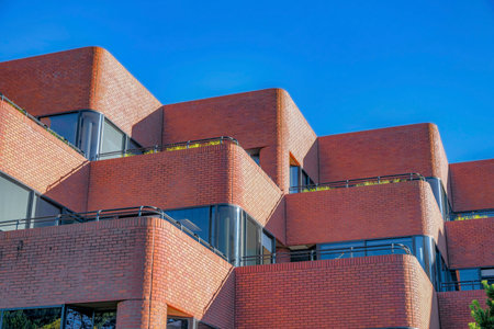 Modern building with red brick wall against blue sky in San Francisco. Large glass windows and glass doors that opens out to the balcony can be seen from the facade.の写真素材