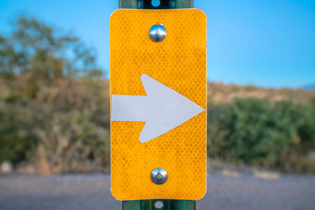 Yellow sign with white right arrow at Sabino Canyon State Park in Tucson, Arizona. Close-up of a posted signage against the blurred desert landscape.の写真素材