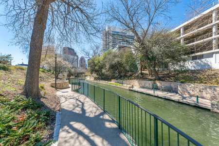 Downtown San Antonio, Texas- River walk near the multi-storey residential buildings. Concrete walkway with leafless trees, lamp posts, and railings near the river.の写真素材