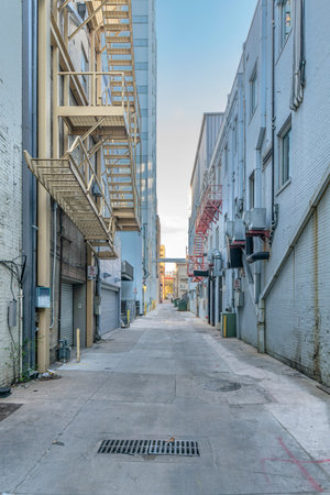 Austin, Texas- Concrete alleyway in between adjacent residential buildings. There are buildings on both side of the alley with emergency stairs and trash cans at the front.の写真素材