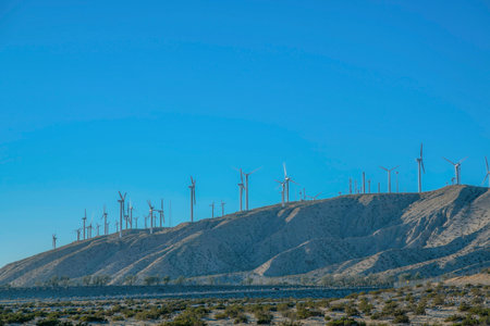 Windmills on top of a mountain in a desert at California. View of wind turbines from desert land with wild plants and a view of a clear blue sky.の写真素材