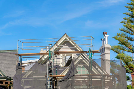 Unfinished house exterior with scaffolding covered with net in San Francisco, California. View of a peak of an under construction house with chimney near the pine tree on the right.の写真素材