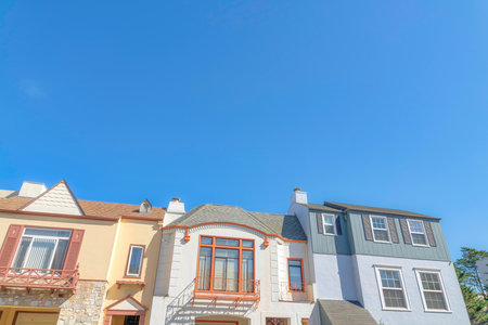 Three houses in a low angle view with different wall sidings in San Francisco, California. There are two houses on the side with fake window shutters and house in the middle with window railings.の写真素材