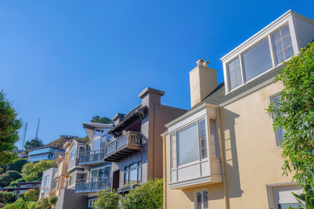 Row of suburban houses near a slope with two towers at the back in San Francisco, California. There is a beige house at the front with bay window along with the houses with balconies.の写真素材