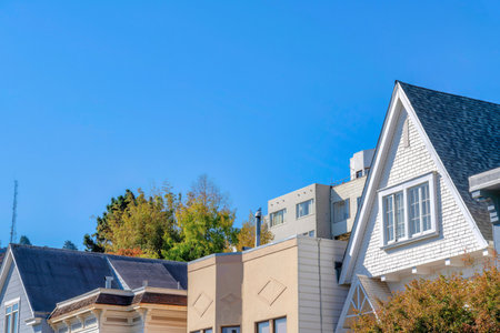 Exterior of top part of the houses in San Francisco, CA. House peaks with different structures and wall sidings with a view of a telecom tower and trees on the left against the sky.の写真素材