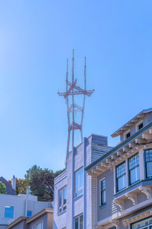 View of Sutro Tower above the houses in San Francisco, CA. There are houses at the front below with different facade exterior and a view of trees on the left at the back.の写真素材