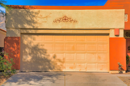 Large sectional garage door with concrete driveway in Tucson, Arizona. Exterior of an attached garage with yellow and orange wall near the front door on the right.の写真素材