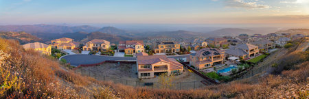 View of a fenced residential area at San Diego, California. Large houses on a cul de sac road against the view of mountains and sky at the background.の写真素材