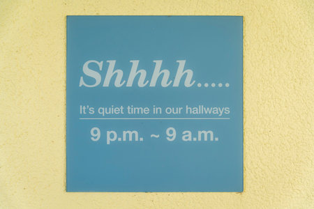 Destin, Florida- Sign on a wall with Shhhh... It's quiet time in our hallways- 9 p.m- 9 a.m. Light blue signage on a painted light yellow wall.の写真素材