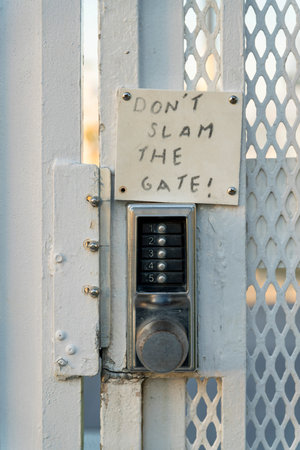 Destin, Florida- Stainless steel key code lock of a gate with Don't slam the gate note. Close-up of a lock of a gate with white metal rails and expanded steel sheet.の写真素材