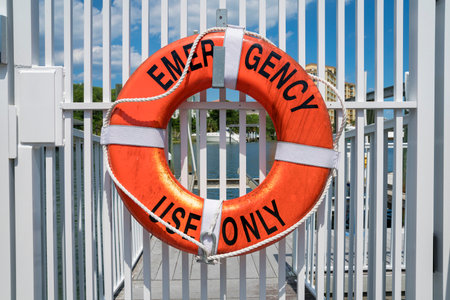 Destin, Florida- Lifebuoy ring with Emergency Use Only lettering. Hanging lifebuoy on a white gate railings against the view of water at the background.の写真素材