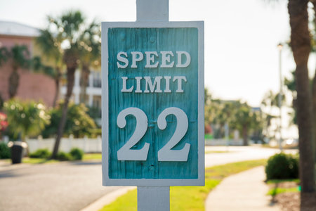 Destin, Florida- Carved road sign with Speed Limit 22. Signage close-up against the view of the sidewalk on the right and grass in between the road on the left.の写真素材