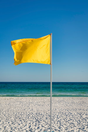 Yellow flag on a pole at the beach in Destin, Florida. Vertical shot of a flag against the view of a white sand and blue ocean and sky at the background.の写真素材