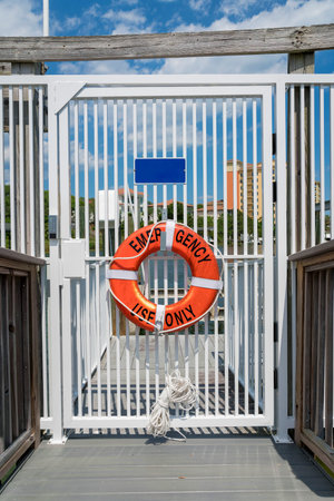 Destin, Florida- Orange lifebuoy with Emergency Use Only hanging on a closed white gate. Lifebuoy on a gate with keypad lock and a view of the dock at the background.の写真素材