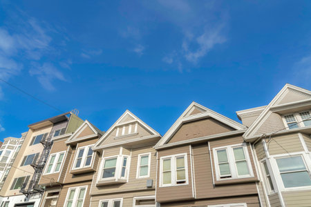 Sloped suburban houses with beige and light brown exterior in San Francisco, California. Complex houses with gable roofs along with the multi-storey apartment on the left in a low angle view.の写真素材