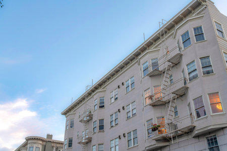 Apartment building with beige exterior and emergency stairs exit in a low angle view. Residential building in San Francisco, California with bay windows against the sky at the background.の写真素材