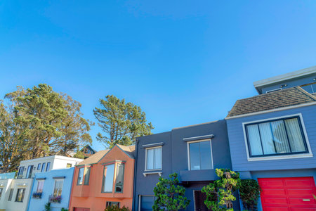 Row of small houses with reflective windows and attached garages in San Francisco, California. Facade of colorful houses against the trees and clear sky background.の写真素材