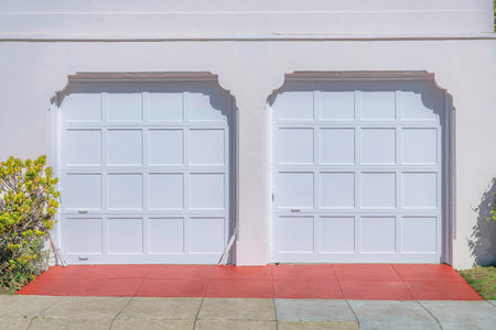Two white sectional garage doors with clipped entrance- San Francisco, California. Two identical garage doors with red concrete driveways with bushes on the side.の写真素材