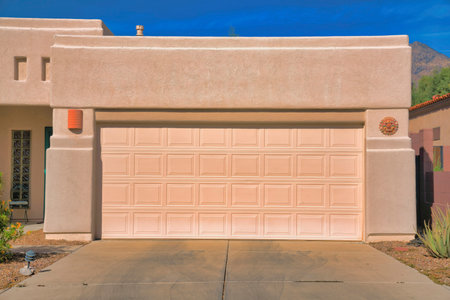 Garage exterior of a painted cream mediterranean home at Tucson, Arizona. There is a concrete driveway at the front of sectional garage doors with wall lights and ornaments on both sides.の写真素材