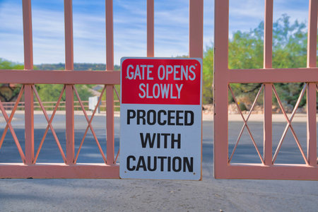 Gate opens slowly Proceed with caution signage on a metal gate at Tucson, Arizona. Close-up of a...