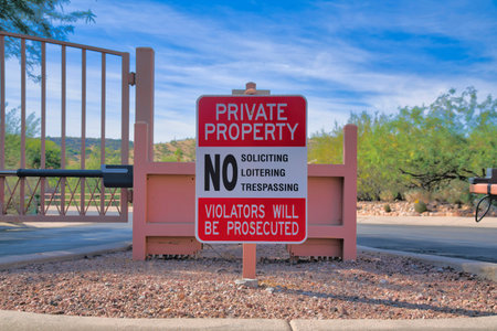 Private property signage on a post near the gate at Tucson, Arizona. No soliciting, no loitering, no tresspassing, violators will be prosecuted written on a signage against the gate and road.の写真素材