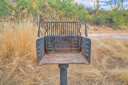 Post-mounted rusty campground grill against a shrubland in Tucson, Arizona. Close-up of an outdoor...