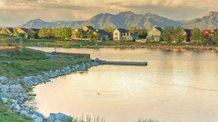 Panorama Panoramic view of the residential area against the mountain range background at Daybreak, Utah. Oquirrh lake waterfront with field and rocks near the shoreline and water with reflection of the sky.の写真素材