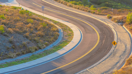 Panorama High angle view of a winding road with road intersection sign at San Diego, California. Winding road on top of a mountain with a view of mountains vast field of bushes and grass.の写真素材